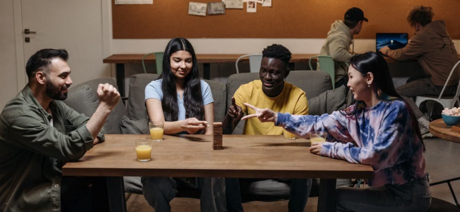 A diverse group of young adults playing Jenga indoors, having fun and connecting over a board game.